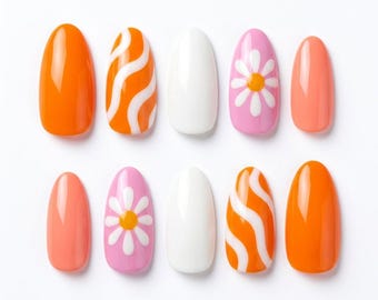 Può includere: Un set di dieci unghie finte a forma di mandorla con finitura lucida. I design includono colori solidi arancione, bianco e corallo, oltre a unghie arancioni con linee ondulate bianche e rosa con una margherita bianca dal centro giallo.