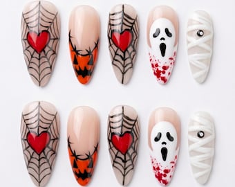 Può includere: Un set di dieci unghie finte a mandorla con decorazioni di Halloween. I motivi includono ragnatele nere con cuori rossi, facce di zucca arancioni, maschere fantasma bianche con schizzi di sangue rosso e bende da mummia su base color carne.