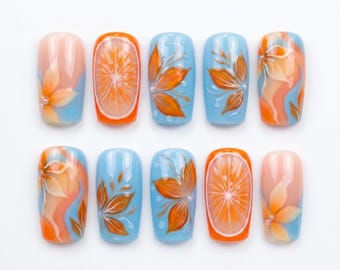 Può includere: Un set di dieci unghie finte con una palette di colori azzurro e arancione. I disegni includono fette di agrumi arancioni dipinte a mano, motivi floreali arancioni e motivi astratti vorticosi con piccoli accenti bianchi su finitura lucida.