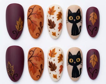 Può includere: Un set di dieci unghie finte a forma di mandorla con un design a tema autunnale. Le unghie presentano basi color viola scuro, arancione e crema decorate con foglie autunnali dipinte, viticci e gatti neri con grandi occhi gialli.