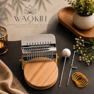 May include: A metal darning loom tool with a round wooden base, featuring a series of silver hooks and a rectangular metal plate. Included are a long metal needle with a white spherical top, a metal hook tool, and several orange rubber bands.