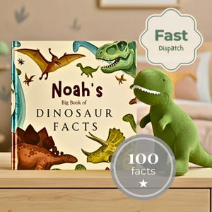 Puede incluir: Un libro de tapa dura titulado Noah's Big Book of DINOSAUR FACTS con ilustraciones coloridas de varios dinosaurios, acompa&ntilde;ado de un peluche verde de Tyrannosaurus Rex sobre una superficie de madera clara.