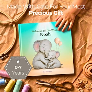 K&ouml;nnte beinhalten: Ein quadratisches Hardcover-Buch mit dem Titel Welcome To The World Noah und einer Aquarellillustration von zwei grauen Elefanten mit rosa Luftballons. Das Cover enth&auml;lt den Text Made With Care For Your Most Precious Gift und ein 0-7 Years Abzeichen.