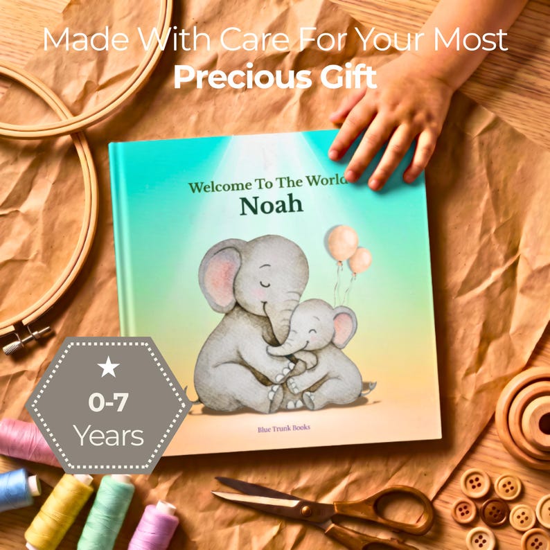 K&ouml;nnte beinhalten: Ein quadratisches Hardcover-Buch mit dem Titel Welcome To The World Noah und einer Aquarellillustration von zwei grauen Elefanten mit rosa Luftballons. Das Cover enth&auml;lt den Text Made With Care For Your Most Precious Gift und ein 0-7 Years Abzeichen.