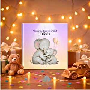 K&ouml;nnte beinhalten: Ein quadratisches Hardcover-Buch mit dem Titel Welcome To The World Olivia, das eine Aquarellillustration eines gro&szlig;en Elefanten zeigt, der ein Elefantenbaby mit zwei Luftballons umarmt. Der Einband ist hellviolett mit dem Text Blue Trunk Books.