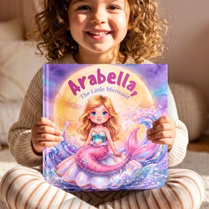 May include: A hardback children's book titled Arabella, The Little Mermaid, featuring a colourful illustration of a blonde mermaid with a pink tail sitting on a large seashell against a yellow moon background with purple and blue water splashes.