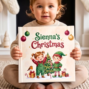 Puede incluir: Un libro cuadrado de tapa dura titulado Sienna's Christmas con una ilustración festiva de un niño y un elfo junto a un árbol de Navidad decorado con regalos, un petirrojo y adornos colgantes sobre un fondo crema con copos de nieve.