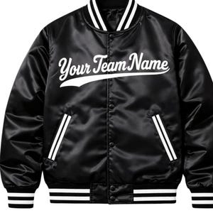 Könnte beinhalten: Schwarze Satin-Bomberjacke mit weißen Akzenten. Auf der Jacke steht in einer Schriftart "Your Team Name". Weiße Streifen zieren Kragen, Manschetten und Taschen. Ein klassischer College-Stil.