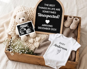 May include: A wooden crate containing a cream-colored teddy bear holding a black and white ultrasound image, a black arched letter board with the text THE BEST THINGS IN LIFE ARE SOMETIMES Unexpected! ARRIVING DECEMBER 202X, baby booties, and a white onesie.