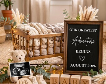 May include: A wooden baby cradle with a cream knit blanket, a teddy bear holding a sonogram, a round sign reading Hello Baby, four wooden blocks spelling BABY, and a framed chalkboard sign reading OUR GREATEST Adventure BEGINS AUGUST 2026.