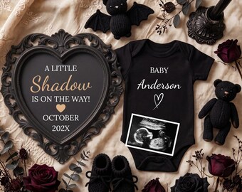 May include: A black baby bodysuit with the text Baby Anderson and a heart, a heart-shaped frame with the text A LITTLE Shadow IS ON THE WAY! OCTOBER 202X, a black crochet bat, a black crochet teddy bear, black booties, and dark red roses.