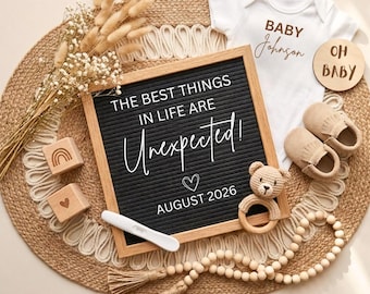 May include: A black felt letter board with a wooden frame displaying the text THE BEST THINGS IN LIFE ARE Unexpected! AUGUST 2026, accompanied by a white baby bodysuit, tan moccasins, a crochet bear rattle, wooden blocks, and dried flowers.