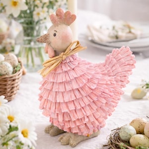 May include: A decorative pink hen figurine with a ruffled body, a light-colored head, and a straw bow around its neck. The hen is part of an Easter-themed table setting, surrounded by eggs and flowers.