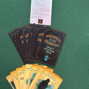 May include: A deck of cards with the title "Whispers in the Shadows: Spirit Question Deck" and other cards with the text "The Storyteller" and "The Spirit's Confession Booth". The cards are on a green surface.