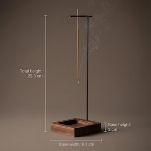 May include: A black metal incense holder with a wooden base. The total height is 10 inches, the base width is 3.6 inches, and the base height is 0.8 inches. An incense stick is lit, with smoke rising. The holder is designed for incense sticks.