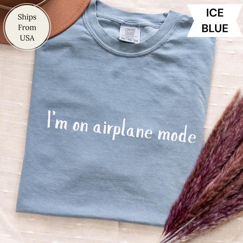 May include: Pale blue t-shirt with the white text "I'm on airplane mode". The shirt is a Comfort Colors brand. The t-shirt is a light blue colour.
