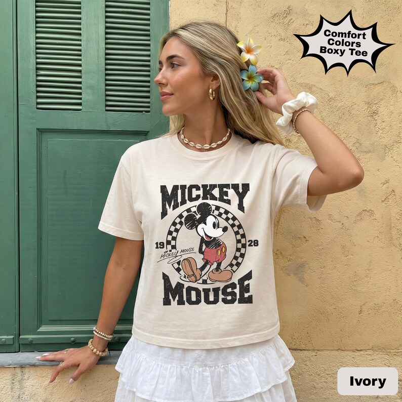 May include: Ivory-colored boxy tee featuring a vintage Mickey Mouse graphic. The design includes the words "Mickey Mouse" in bold letters, along with the years "19" and "28". The shirt is labeled "Comfort Colors Boxy Tee".