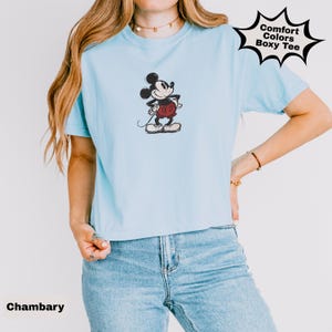 May include: Pale blue Comfort Colors Boxy Tee with a sketched Mickey Mouse design. The shirt has short sleeves and a crew neck. The word "Chambary" is printed at the bottom left.