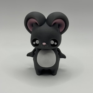 Könnte beinhalten: Eine 3D-gedruckte Figur einer Cartoon-Maus. Die Maus ist hauptsächlich dunkelgrau mit großen, runden Augen, einer rosa Nase und rosa Innenohren. Sie hat einen weißen Bauch und kleine Arme. Die Figur ist zum Aufrechtstehen konzipiert.