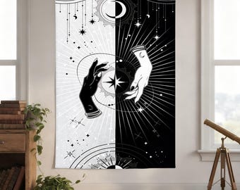 May include: Black and white tapestry featuring a celestial design. The tapestry is split vertically, with one side black and the other white. Each side has a hand reaching towards a central star. The design includes moons, stars, and suns.