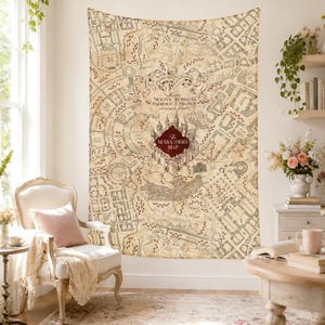 Puede incluir: Un gran tapiz con un diseño de mapa detallado con el texto "The Marauders Map". El mapa está en tonos beige y marrón, con un emblema de castillo burdeos. El tapiz está colgado en una pared blanca.
