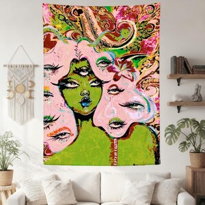 May include: A vibrant tapestry featuring a surreal illustration of a woman with multiple eyes and a green complexion. The artwork incorporates pink, green, and paisley patterns, creating a psychedelic aesthetic. The tapestry is displayed on a white wall above a white sofa.