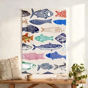 May include: A rectangular wall hanging featuring a repeating pattern of colorful fish illustrations. The fish are in various colors, including blue, red, green, and pink, against a cream-colored background. The artwork is displayed above a wooden bench with a pillow, mug, and books.