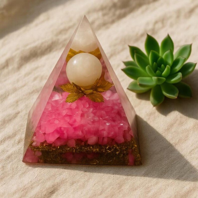 Side view of the Rose Quartz Orgone Pyramid, showcasing the distinct layers of energy-conducting materials. The golden base sparkles under the light, illustrating the artisan craftsmanship and the spiritual intention behind this EMF protection device.