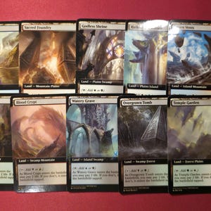 Pode incluir: Uma cole&ccedil;&atilde;o de dez cartas colecion&aacute;veis de Magic: The Gathering. Cada carta apresenta obras de arte &uacute;nicas retratando paisagens e estruturas. As cartas s&atilde;o rotuladas com nomes como "Breeding Pool" e "Sacred Foundry."