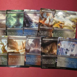 Pode incluir: Uma cole&ccedil;&atilde;o de cartas colecion&aacute;veis Magic: The Gathering, apresentando v&aacute;rias cartas de terreno com arte de paisagens. As cartas exibem nomes como "Marsh Flats" e "Verdant Catacombs" com ilustra&ccedil;&otilde;es e texto detalhados. As cartas est&atilde;o dispostas em uma superf&iacute;cie vermelha.