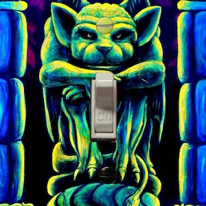 May include: A unique light switch cover featuring a gargoyle design in shades of blue and yellow. The switch is in the 'ON' position. The artwork has a fantasy theme and is set against a dark background.