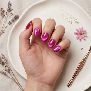 May include: A hand with magenta cat-eye gel nails. The nails are oval-shaped and glossy. The image includes a white plate with text, a nail tool, and lavender sprigs.