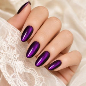 Pode incluir: Unhas de formato oval com um verniz roxo profundo com efeito metálico de olho de gato. As unhas apresentam um brilho magnético refletor que cria uma linha vertical de luz brilhante no centro de cada superfície da unha violeta escura.