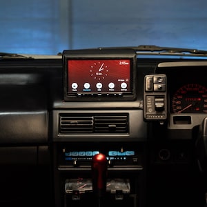 May include: A car dashboard featuring a red-screen Sony car stereo displaying the time and date. The dashboard is black with various controls, gauges, and a red gear shift knob. The speedometer reads 60 mph.