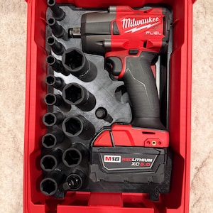May include: Red Milwaukee FUEL impact wrench and socket set in a red case. The set includes various black sockets and a M18 REDLITHIUM XC5.0 battery. The case is open, revealing the tools neatly organized.