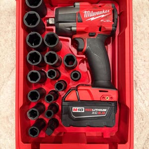 May include: A red Milwaukee FUEL impact wrench and socket set in a red case. The set includes various black sockets and a red and black battery pack. The case is open, revealing the tools neatly arranged inside.