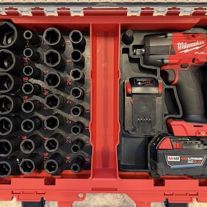 Könnte beinhalten: Ein roter Werkzeugkoffer mit einem schwarzen und roten Milwaukee FUEL Schlagschrauber, zwei Akkus und einem Satz schwarzer Steckschlüssel. Die Steckschlüssel sind in einem Raster angeordnet, mit Größenangaben. Der Koffer ist geöffnet und zeigt die Werkzeuge.