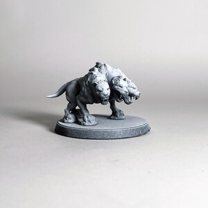 May include: A gray, three-headed Cerberus figurine, standing on a circular base. The mythical creature has a lion-like body with three snarling heads and is sculpted in a detailed, realistic style. The figurine is a fantasy-themed collectible.