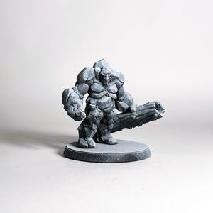 May include: A gray stone-like figurine of a humanoid creature with a club. The figure has a textured, rocky appearance and stands on a circular base. The creature's pose suggests strength and readiness.