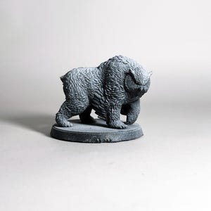 May include: A gray, textured sculpture of a bear-like creature with a round base. The sculpture has detailed fur and a stern expression. The artwork is a decorative item.