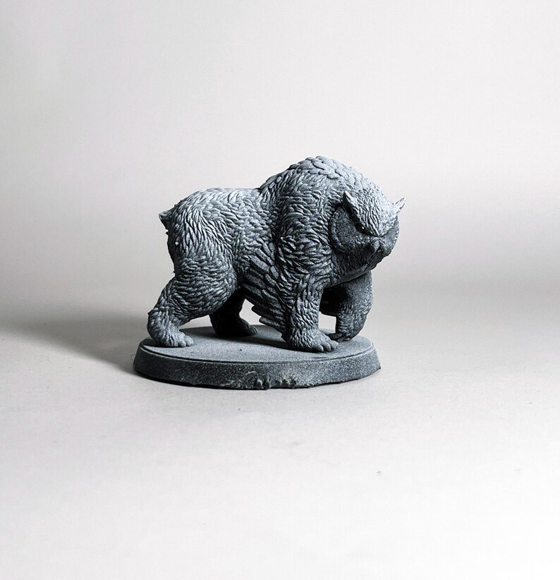 May include: A gray, textured sculpture of a bear-like creature with a round base. The sculpture has detailed fur and a stern expression. The artwork is a decorative item.