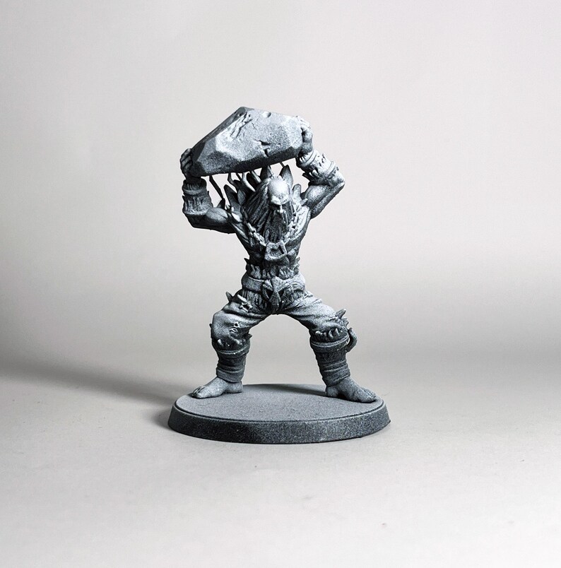 May include: A gray figurine of a muscular humanoid figure holding a large rock overhead. The figure is detailed with textured clothing, a beard, and spiked accents. It stands on a circular base.