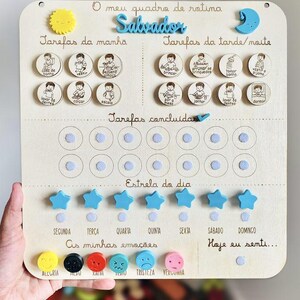 Könnte beinhalten: Tägliche Routine-Tafel aus Holz mit dem Namen "Salvador" in Blau. Sie zeigt illustrierte Aufgaben, sternförmige Belohnungsmagnete und Emotionsindikatoren. Die Tafel soll Kindern helfen, ihre täglichen Aktivitäten zu verwalten.