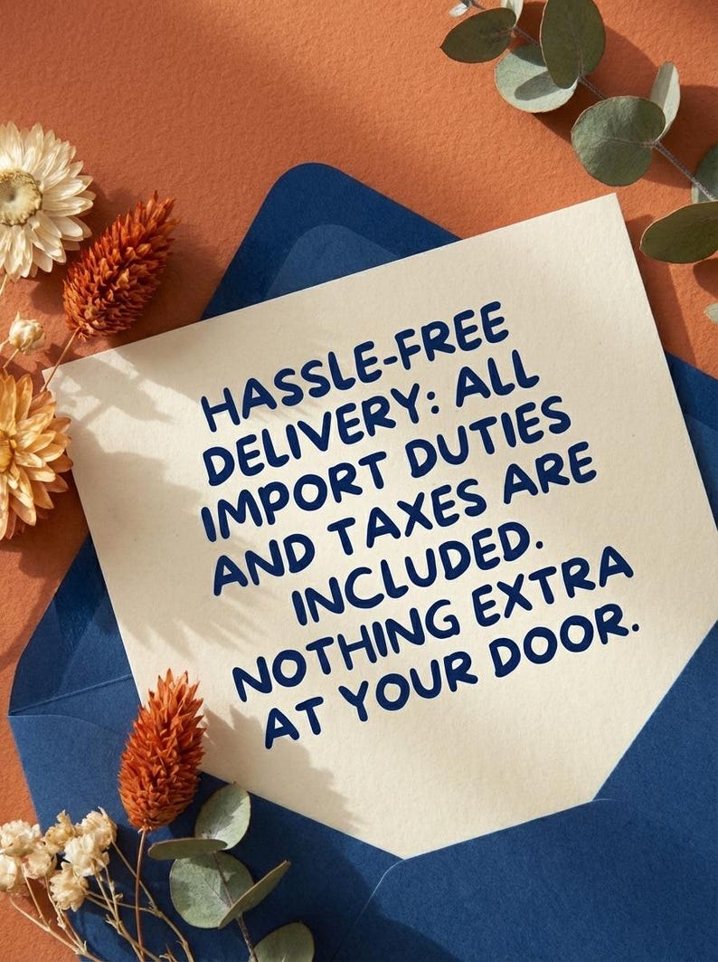 May include: A cream-colored card with blue text that reads "HASSLE-FREE DELIVERY: ALL IMPORT DUTIES AND TAXES ARE INCLUDED. NOTHING EXTRA AT YOUR DOOR." The card is inside a blue envelope, with dried flowers and greenery.