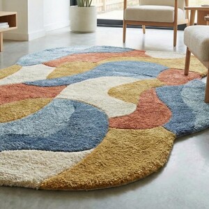 May include: A colorful, abstract area rug with a soft, textured surface. The rug features a flowing design with sections of blue, orange, yellow, and cream colors. The rug is an oval shape and appears to be made of a plush material.