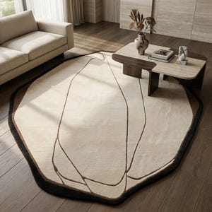 Può includere: Un tappeto dalla forma organica irregolare caratterizzato da un ampio centro color crema con sottili motivi a linee astratte marrone scuro. Il tappeto presenta un bordo spesso marrone scuro che segue il suo perimetro asimmetrico.