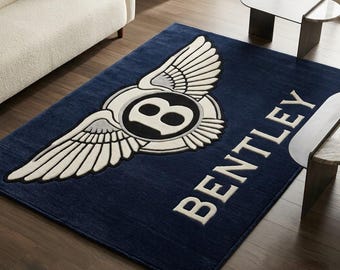 May include: A rectangular area rug in deep navy blue featuring the white and black Bentley winged logo centered on the surface. The word BENTLEY is written in large, bold, white capital letters positioned diagonally across the lower right corner.