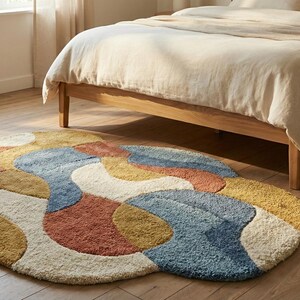 May include: A colorful, abstract rug with a wavy design in shades of blue, orange, yellow, and cream. The rug is placed on a wooden floor near a bed with a light-colored comforter. The rug's dimensions are approximately 60 inches in diameter.