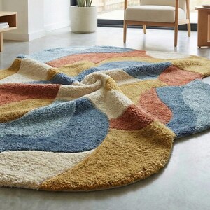 May include: A colorful, abstract area rug with a soft, textured surface. The rug features a pattern of overlapping shapes in shades of blue, orange, yellow, and cream. The rug is designed to add a modern touch to any living space.