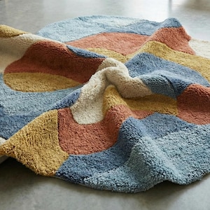 May include: A colorful, abstract rug with a soft, textured surface. The rug features a patchwork design with sections of blue, yellow, orange, and cream. The rug is approximately 60 inches in diameter, perfect for a living room or bedroom.